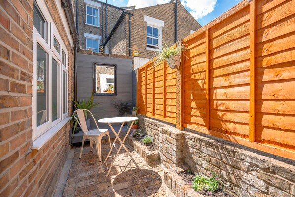 A brick house with a wooden fence, a small garden with plants, a white chair, and a table. - Rare 5 bed House in Vauxhall With Roof Terrace (London)