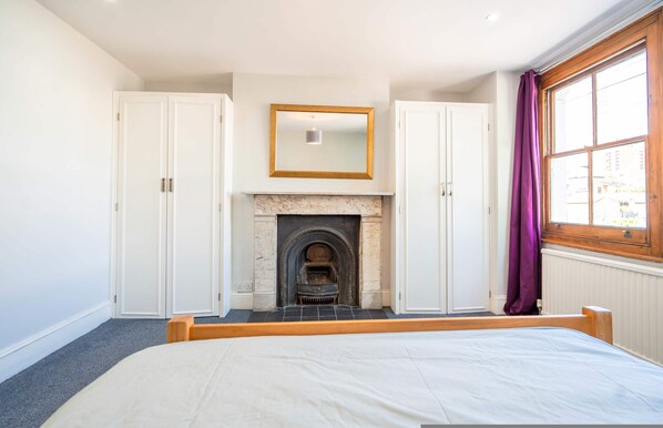 Ein Schlafzimmer mit einem Bett, Kamin, weißen Schränken und einem Fenster mit Vorhängen.