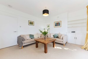 A living room with a wooden coffee table, beige sofa, white walls, and a ceiling light fixture. - Spacious Duplex 3 bed on the Southbank (London)