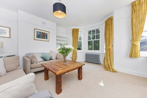 A living room with a wooden coffee table, beige sofa, and yellow curtains. - Spacious Duplex 3 bed on the Southbank (London)