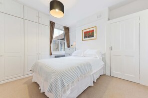 A bedroom with a bed, white wardrobe, a window with curtains, a radiator, and a framed picture on the wall. - Spacious Duplex 3 bed on the Southbank (London)
