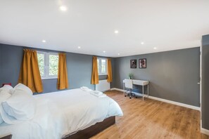 Quarto com cama, duas janelas com cortinas, uma escrivaninha e um radiador.