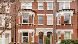 Une maison de ville en briques rouges, avec des éléments décoratifs blancs, de nombreuses fenêtres et une porte d’entrée.