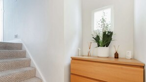 Un escalier menant à une pièce où se trouvent une commode en bois, une plante en pot et une fenêtre.