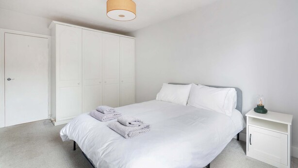 Une chambre à coucher comprenant un lit, une table de chevet, une armoire et un luminaire suspendu.
