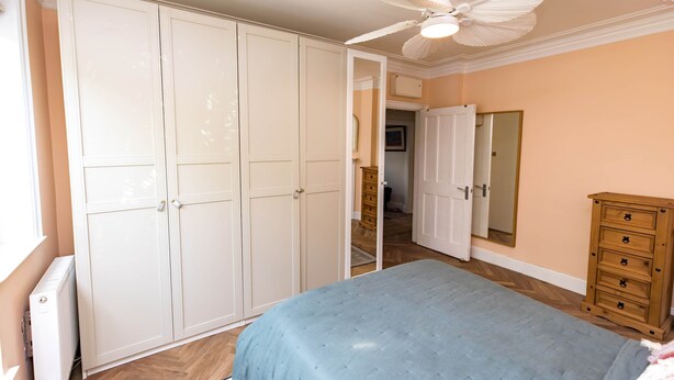 A bedroom with a bed, a wardrobe, a dresser, a ceiling fan, and a mirror. - Beautiful Earlsfield Home With Garden (London)