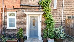 A brick house with a grey door, white window frames, and a small garden with potted plants. - Beautiful Earlsfield Home With Garden (London)