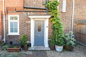 A brick house with a grey door, white window frames, and a small garden with potted plants. - Beautiful Earlsfield Home With Garden (London)