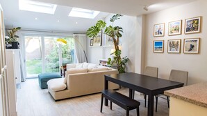 A modern living room with a sofa, a dining table, and a bench. There are potted plants and framed pictures on the walls. - Beautiful Earlsfield Home With Garden (London)