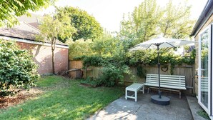A patio area with a bench, an umbrella, and a wooden fence. - Beautiful Earlsfield Home With Garden (London)