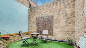 Un patio con dos sillas, una mesita, un muro decorativo y un muro de ladrillo.
