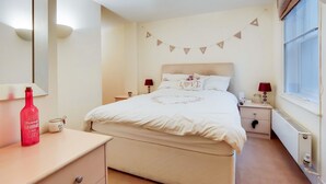 Un dormitorio ordenado con cama, mesitas de noche, un espejo, una ventana y una lámpara fijada a la pared.
