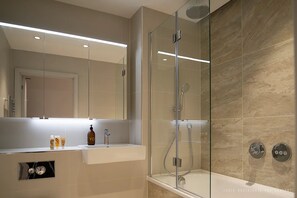 Un baño moderno con ducha envuelta en vidrio, tocador con espejo y bañera.