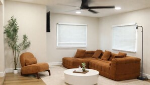 Una sala de estar con un sofá marrón, una mesa de centro blanca, una lámpara de pie y un ventilador de techo.