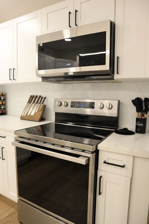 Una cocina con electrodomésticos de acero inoxidable, armarios blancos y un juego de cuchillos.