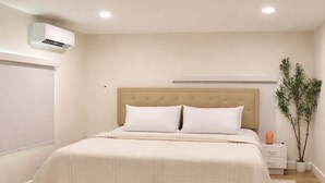 Un dormitorio con cama, mesita de noche, planta en maceta y equipo de aire acondicionado.