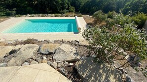 Ein rechteckiger Pool mit klarem, blauem Wasser, umgeben von einer Steindeck und einer natürlichen Landschaft mit Bäumen und Bergen im Hintergrund.