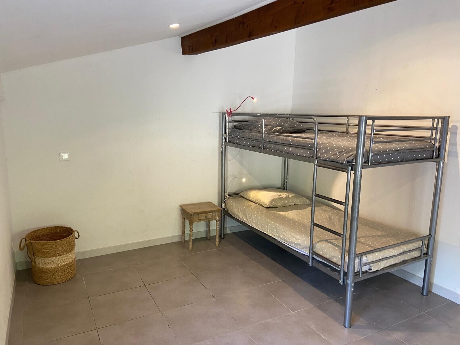 Ein Stockbett in einem Zimmer, mit einem kleinen Holzschemel und einem gewebten Korb.