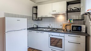 A compact kitchen with white cabinets, a gas stove, a microwave, and a refrigerator.