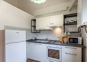 Una cucina compatta con mobili bianchi, un fornello a gas, un forno a microonde e un frigorifero.