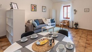 A cozy living room with a sofa, a coffee table, and a dining area with chairs and a table set for tea.