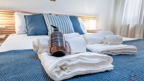 A neatly made bed with folded towels, a bottle of shampoo, and a striped pillow.
