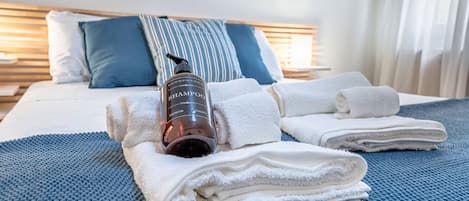 A neatly made bed with folded towels, a bottle of shampoo, and a striped pillow.