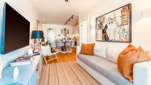 A modern living room with a sofa, a flat-screen TV, a dining area, and a kitchen in the background. - Sage Sea Point 1 Bed Ocean View (Cape Town)
