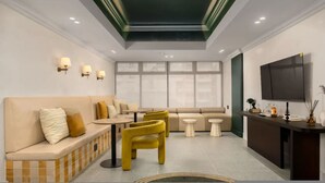 A modern hotel room with a sofa, yellow chairs, a small table, a TV, and a window. - Sage Sea Point 1 Bed Ocean View (Cape Town)