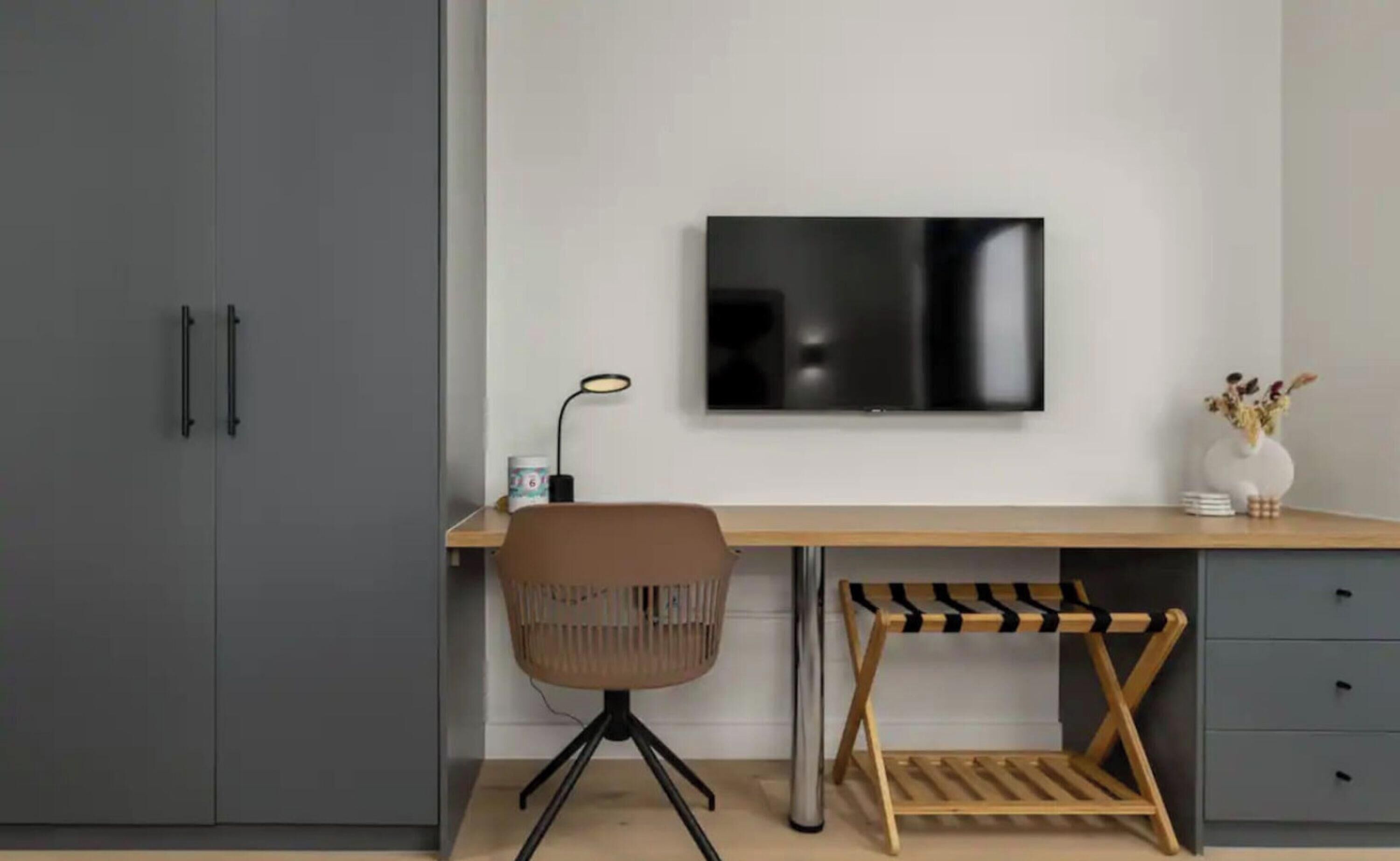 A modern office space with a desk, chair, TV, and storage cabinets.