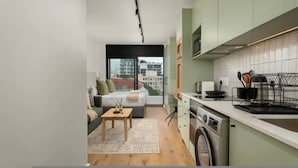 Ett kompakt bostadsutrymme med en soffa, ett litet bord, en tvättmaskin och ett litet kök.