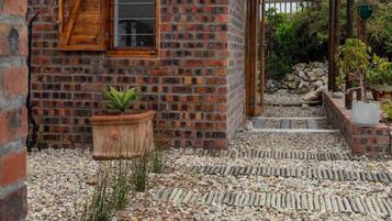 A brick building with a wooden door, a potted plant, and a gravel pathway leading to a covered area.