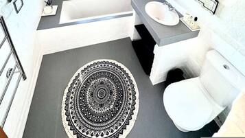 A modern bathroom with a bathtub, sink, toilet, and a large mirror.