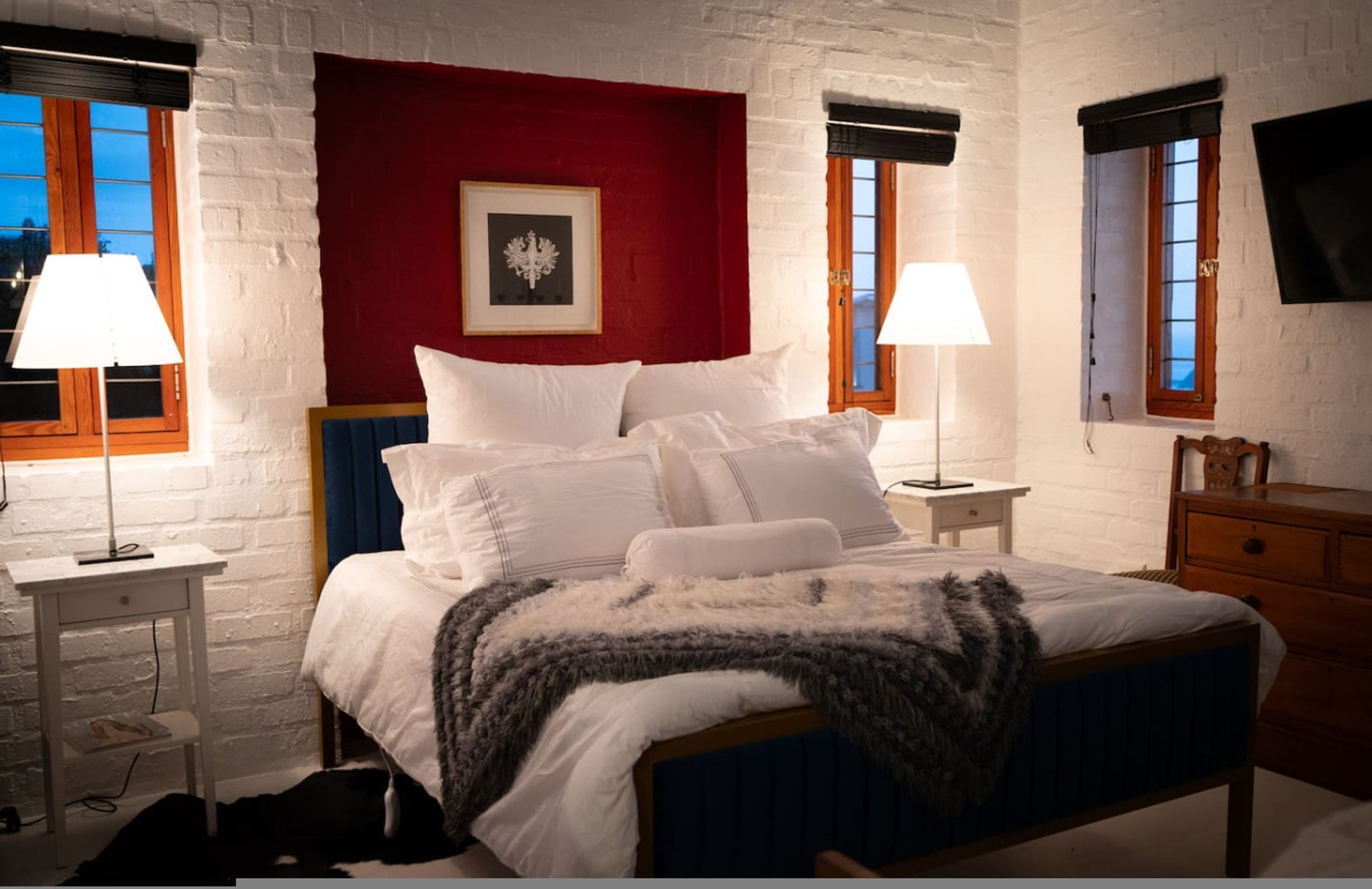 A bedroom with a bed, two bedside tables, a nightstand, a dresser, and a television on the wall.