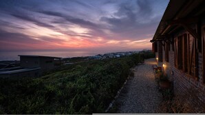 A building with a sloped roof, a gravel pathway, and a view of the sea at dusk. - Yzerfontein 3 Bed House With Pool Sea Views (Yzerfontein)