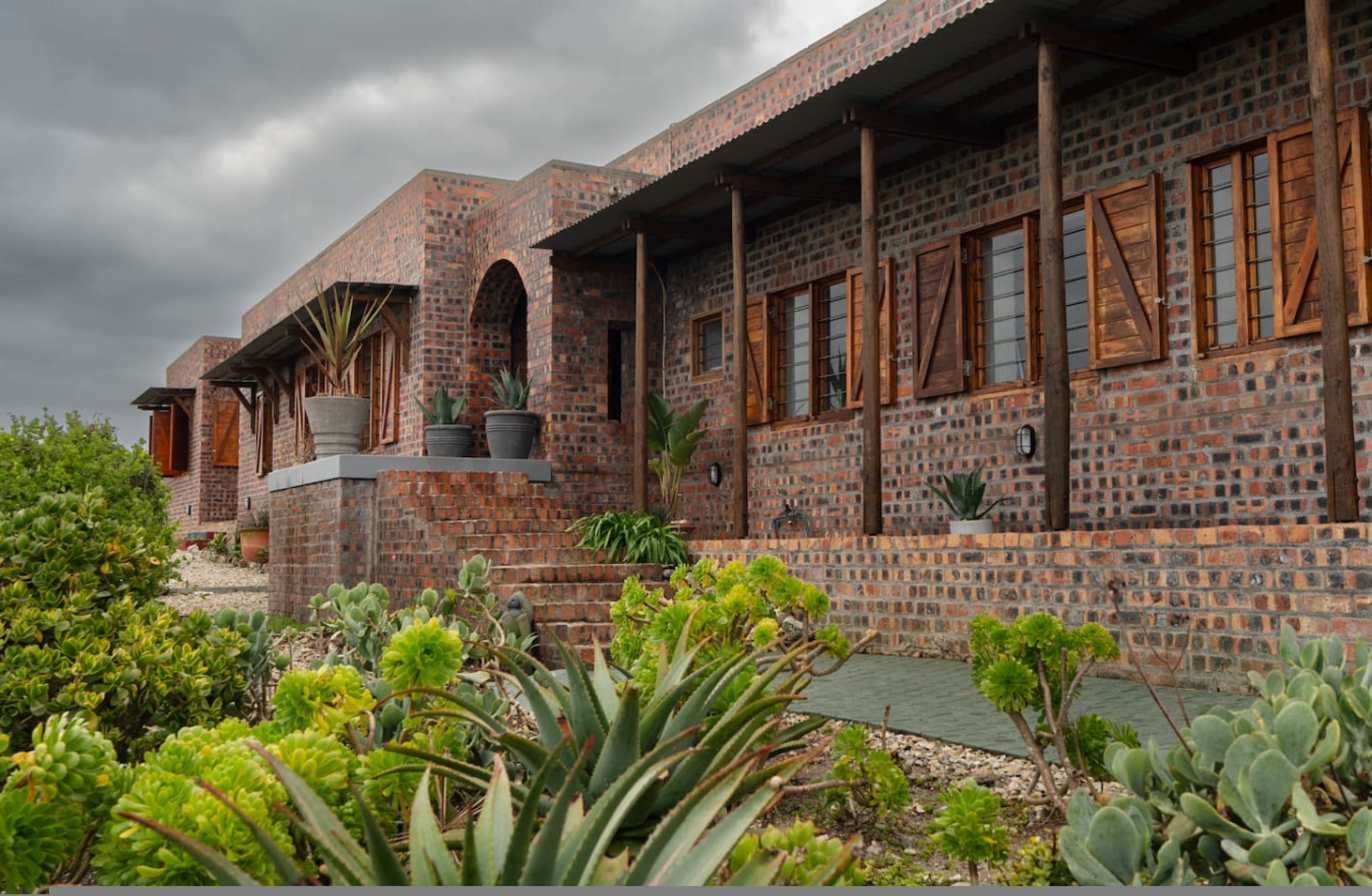 A brick building with arched windows and a balcony with potted plants.
