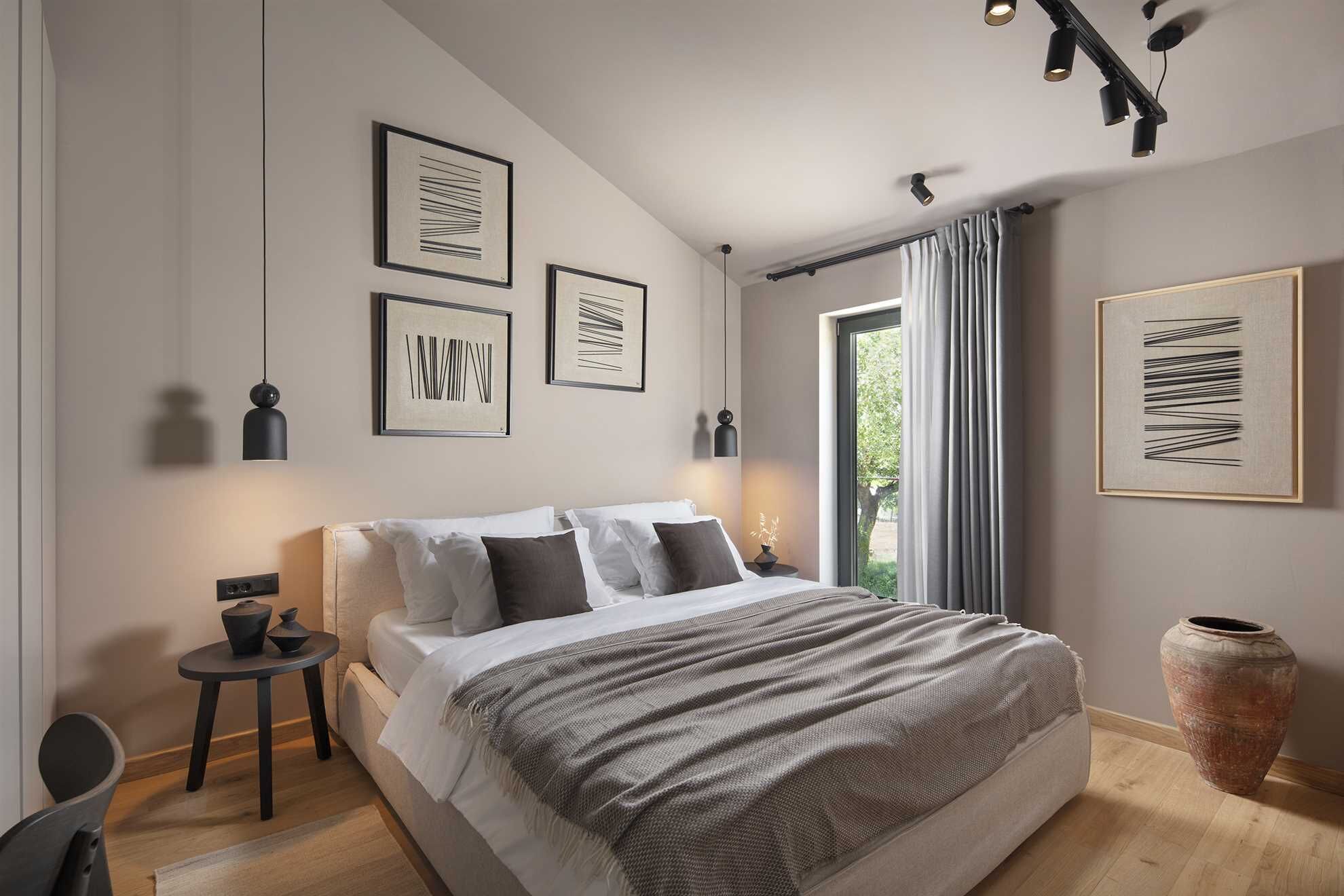 A modern bedroom with a bed, bedside tables, artwork, and a large window.