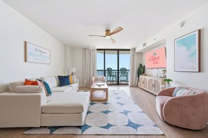 A modern living room with a sofa, armchair, and coffee table, a ceiling fan, and a view to a balcony. - Ocean Front Condo- Indoor & Outdoor Pools- Lazy River + Hot Tub (North Myrtle Beach)