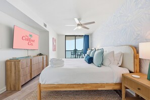A hotel room with a bed, a TV on the wall, a ceiling fan, and a view of the outdoors. - Ocean Front Condo- Indoor & Outdoor Pools- Lazy River + Hot Tub (North Myrtle Beach)