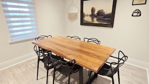A dining room with a wooden table and black chairs, a framed picture on the wall, and a window with blinds. - 3BR home w/ large yard near wineries & outlet (Niagara-on-the-Lake)