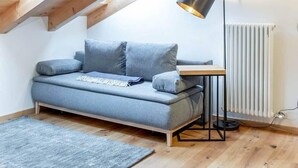 Une chambre à coucher aménagée dans un espace mansardé, avec un plafond en pente, un canapé gris, une petite table, une lampe sur pied et un radiateur.