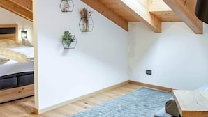 Une pièce avec un plafond en pente, des poutres en bois, une lucarne, un lit, une table et deux éléments de décoration hexagonaux fixés au mur.