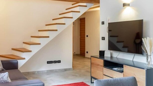 Un salon moderne avec un escalier en bois, un téléviseur à écran plat et une moquette rouge.