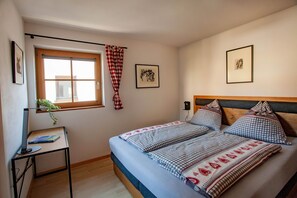 Ein Schlafzimmer mit einem Bett, einem Schreibtisch, einem Fenster mit Vorhängen und zwei gerahmten Bildern an der Wand.