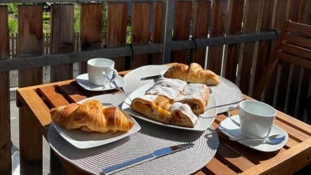 A wooden table with croissants and a cup, overlooking a mountain view. - Apart Vinschgau (Val Venosta) - charming, cozy apartment with mountain view (Laudes)
