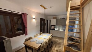 A compact kitchen with a dining area, wooden staircase, and a window with curtains. - Chalet Valmalenco - Valtellina (Provincia di Sondrio)