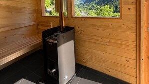 A sauna room with wooden walls, a sauna unit, and a window with a mountain view. - Chalet Valmalenco - Valtellina (Provincia di Sondrio)