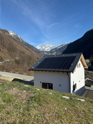 Una pequeña casa blanca con techo de paneles solares, rodeada de montañas y un cielo despejado.