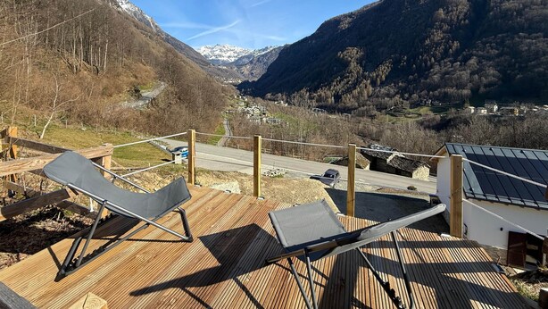 A wooden deck with two lounge chairs, a view of a valley with mountains, and a road leading into the distance. - Chalet Valmalenco - Valtellina (Provincia di Sondrio)