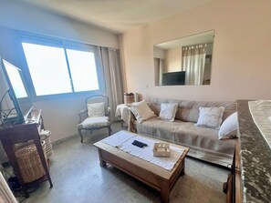 A room with a sofa, armchair, and a table with a laptop and remote control. - Riviera Beauty, Sun & Sea 80 m² close to the Mediterranean 4 pers, Clim, Pkg (Cagnes-sur-Mer)